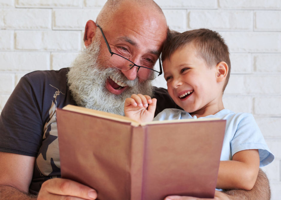 Bearded aged man and his grandson having fun reading a book toge